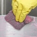 A person wearing yellow gloves using a Scrubble steel wool soap pad to clean a sponge.