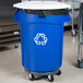 A blue Rubbermaid BRUTE recycling can with white lid and dolly.