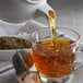 A glass of tea being poured from a tea strainer.