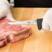 A person in gloves using a Victorinox poultry boning knife to cut meat on a counter.