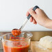 A person using a Vollrath Jacob's Pride ladle to pour red sauce into a measuring cup.