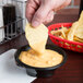 A person dipping a potato chip into a bowl of cheese sauce.