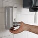 A hand pressing a silver Lavex stainless steel foaming soap dispenser on a wall.