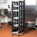A black Rubbermaid Max System steam table pan rack filled with trays in a kitchen.