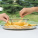 Two hands reaching into a bowl of chips on a white table.
