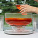 A hand pouring orange liquid into a glass bowl.