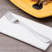 A Chef & Sommelier Renzo stainless steel dinner fork on a napkin next to a plate of food.
