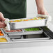 A person holding a Hatco stainless steel food pan over a countertop.