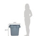 A woman standing next to a Rubbermaid grey square trash can with two handles.