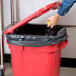 A person snapping a black lid onto a red Rubbermaid trash can.
