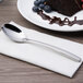 A Chef & Sommelier stainless steel dessert spoon on a napkin next to a piece of chocolate cake.