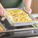 A person holding a Hatco stainless steel food pan full of food in front of a countertop