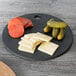 An Epicurean slate wood fiber pizza board with cheese, pickles, and pepperoni on a table.
