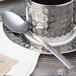 An Arcoroc stainless steel teaspoon on a saucer with a tea bag.