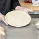 A person in gloves holding a round pizza dough over a round white table.