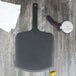 An Epicurean Richlite wood pizza peel with a black handle on a wood surface.
