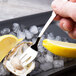 A hand holding an Arcoroc stainless steel oyster fork over an oyster with lemon on ice.