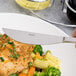An Arcoroc stainless steel dinner knife being used to cut food on a plate.