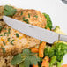 An Arcoroc stainless steel dinner knife on a plate of food with rice, chicken and vegetables.