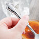 A hand holding a Libbey Lady Astor stainless steel teaspoon.