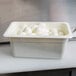 A white Cambro plastic food pan filled with hard boiled eggs on a counter.