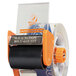 A Duck Tape pistol grip tape dispenser with an orange plastic covering on the handle and an orange and black label.