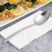 An Arcoroc stainless steel dinner spoon on a plate of food.