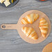 An Epicurean round pizza board with croissants on it on a table.