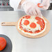 A person wearing gloves puts pepperoni on a pizza on an Epicurean round pizza board.