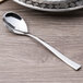 An Arcoroc stainless steel demitasse spoon with a silver handle on a table.