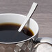 An Arcoroc stainless steel demitasse spoon in a cup of coffee on a counter.