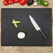 An Epicurean slate Richlite wood fiber cutting board on a counter with a knife and vegetables.