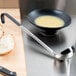 A bowl of soup and a Vollrath Jacob's Pride ladle with a black Kool-Touch handle on a cutting board.