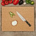 An Epicurean wood fiber cutting board with vegetables and a knife on it.
