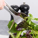 A person using an Arcoroc stainless steel serving fork to serve salad