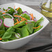 A Schonwald white porcelain bowl filled with salad with spinach, radishes, and carrots.