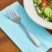 A Choice medium weight stainless steel salad fork on a blue napkin next to a bowl of salad.