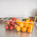 A Carlisle clear polycarbonate food pan filled with fruit sits on a counter.