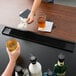 A black bar mat on a counter with a glass of beer and money.