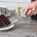 A hand using an Arcoroc stainless steel cake server to cut a piece of chocolate cake on a plate.