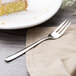 An Arcoroc stainless steel cake fork on a napkin with a piece of cake.