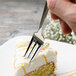 An Arcoroc stainless steel cake fork cutting a piece of cake.