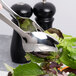 A stainless steel serving spoon with a leafy vegetable in it on a table with other serving utensils.