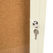 The ivory Aarco Bulletin Board Cabinet with a key in the door.