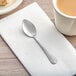 A Choice Dominion stainless steel demitasse spoon on a napkin next to a cup of coffee.