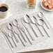 A group of Choice Windsor stainless steel teaspoons on a table with coffee.