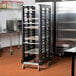 A black Rubbermaid sheet pan rack in a kitchen with sheet pans on it.