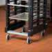 A black Rubbermaid Max System sheet pan rack on a silver cart with wheels.