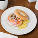 A Schonwald continental white porcelain plate with a bagel, salmon, and onions on a table.
