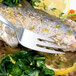An Arcoroc stainless steel fish fork next to a plate of fish with vegetables and a lemon.